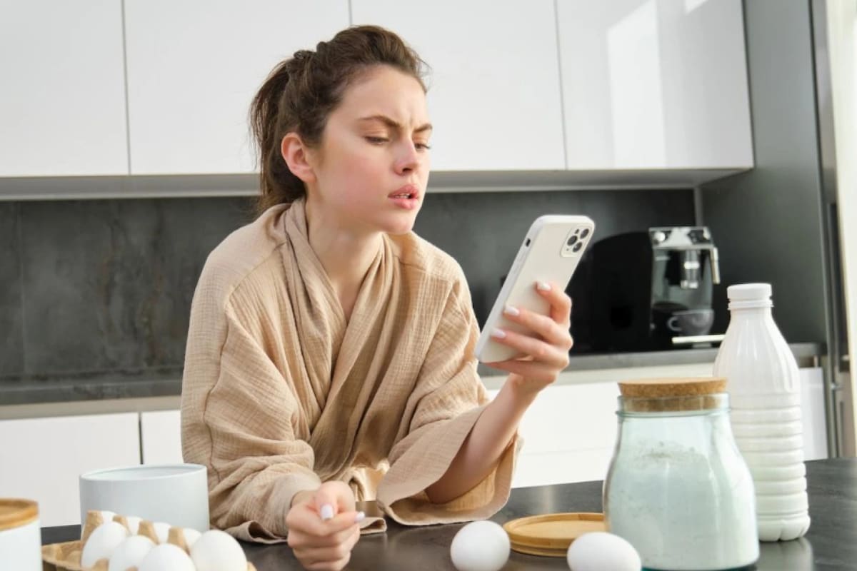 Mujer mira el celular mientras cocina