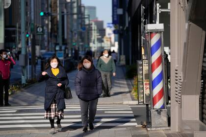 Mujeres con mascarillas para el coronavirus caminan por una calle en Tokio el 9 de febrero del 2022. El primer ministro de Japón Fumio Kishida anunció el miércoles planes para mantener las restricciones por el coronavirus en Tokio y otras 12 áreas por tres semanas más hasta inicios de marzo, en momentos en que las infecciones con ómicron no dan indicio de amainar y la mayoría de los japoneses aún no han recibido el refuerzo de sus vacunas.  (AP Foto/Hiro Komae)