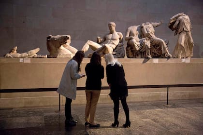 Mujeres están paradas junto una estatua de mármol de un joven desnudo que se cree representa al dios griego Dionisos, centro, desde el frontón este del Partenón, en exhibición durante una oportunidad mediática para promocionar la próxima exhibición del cuerpo humano en arte griego antiguo en el Museo Británico en Londres, el jueves 8 de enero de 2015. (AP Foto/Matt Dunham, Archivo)
