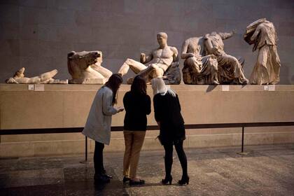 Mujeres frente a una escultura de mármol de un joven desnudo, considerada una representación del dios griego Dionisios, centro, del frontón este del Partenón, exhibida en el Museo Británico