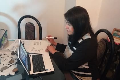 Nancy Sánchez en clase virtual con sus alumnos, preparando el "pizarrón" que arma con hojas para mostrarles en la pantalla.
