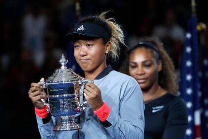 Naomi Osaka posa con el trofeo que ganó tras derrotar a Serena Willims (detrás suyo) en la final del US Open el 8 de septiembre del 2018. (AP Photo/Adam Hunger, File)