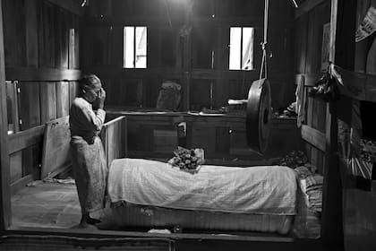 Ne Selpi, 80 años, se persigna después de depositar la comida al costado de un ataúd que contiene el cuerpo de su hermana Norma en el interior del Tongkonan, la casa tradicional que precede al resto de construcciones en el recinto familiar en el poblado de Deri.