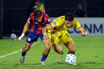 Nicolás Tripichio y Kevin Parzajuk prácticamente se caen en plena puja por la pelota, en una cierta alegoría del encuentro entre Recoleta y San Lorenzo por la Copa Sudamericana en Paraguay.
