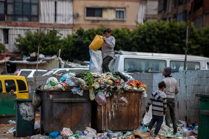 Niños buscan algo de valor en la basura junto a un mercado en Beirut, Líbano, el lunes 12 de abril de 2021. (AP Foto/Hassan Ammar, Archivo)