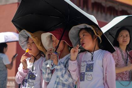 Niños con gorras para sol y paraguas posan para una foto cerca de la Ciudad Prohibida en una jornada de calor sofocante en Beijing, viernes 7 de julio de 2023. (AP Foto/Andy Wong)
