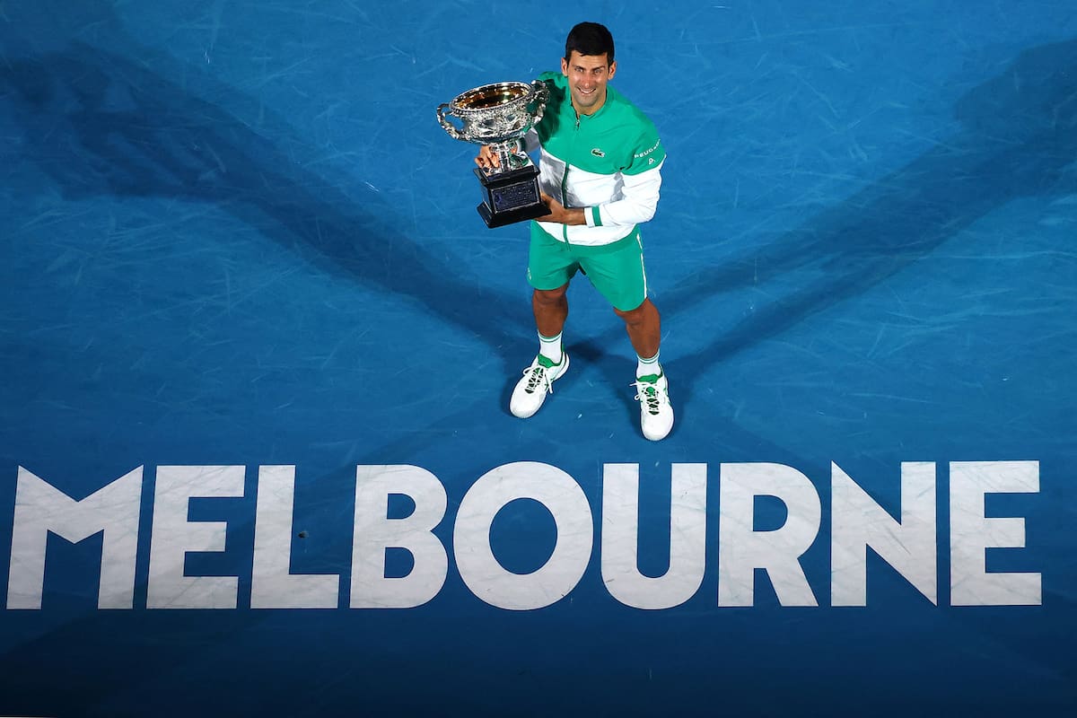 Novak Djokovic y el trofeo del Open australiano que alzó en 2021; el serbio busca festejar una vez más en Melbourne
