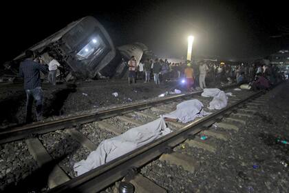 Numerosos cadáveres cubiertos permanecen a un lado de las vías, el sábado 3 de junio de 2023, cerca de donde se descarrilaron dos trenes de pasajeros en el distrito de Balasore, estado de Odisha, en el este de India. (AP Foto)