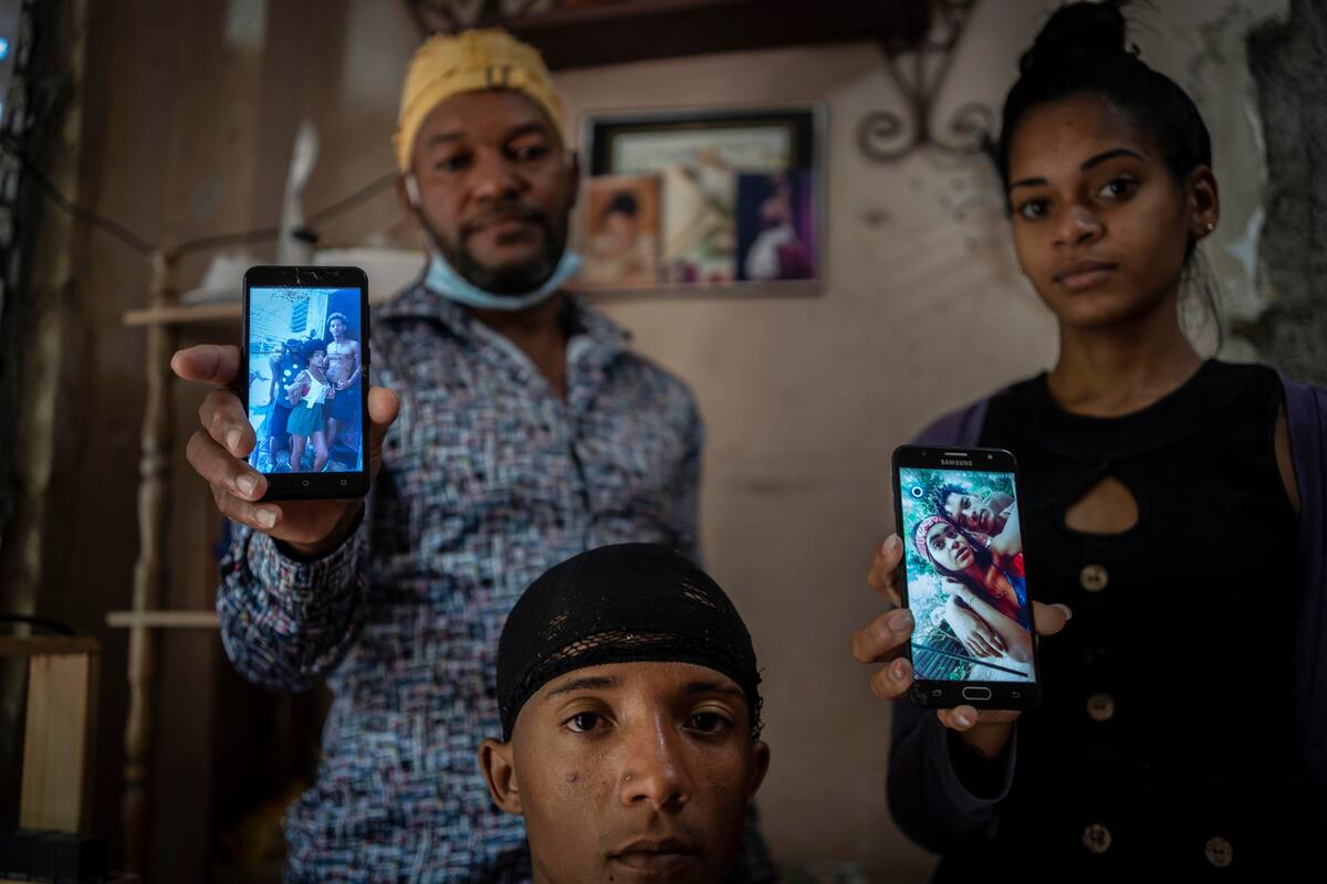 Odlanier Santiago Rodríguez, al centro, quien fue acusado de participar en las protestas de julio del año pasado y fue liberado tras 22 días en prisión, posa para una fotografía junto con su tío Emilio Román, a la izquierda, y la nuera de éste, María Carla Milán Ramos, mientras muestran fotos de los tres hijos de Román que aún permanecen detenidos. La imagen fue tomada en el barrio La Güinera en La Habana, Cuba, el miércoles 19 de enero de 2022 (AP Foto/Ramón Espinosa)