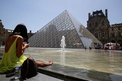 Una mujer se sienta cerca de una fuente frente a la Pirámide del Louvre en París el 17 de junio de 2022, mientras una ola de calor arrasa gran parte de Francia