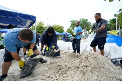 Operarios municipales llenan sacos de arena en un puesto de reparto a residentes antes de la llegada de las lluvias asociadas a la depresión tropical Fred, el 13 de agosto de 2021, en Grapeland Park, Miami. (AP Foto/Wilfredo Lee)