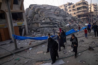 Palestinos caminan junto a un edificio en ruinas tras un ataque aéreo palestino en Ciudad de Gaza, el sábado 8 de octubre de 2023