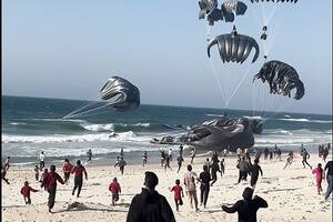 Palestinos corriendo hacia paracaídas sujetos a paquetes de alimentos, lanzados desde aviones estadounidenses en una playa de la Franja de Gaza el 2 de marzo de 2024