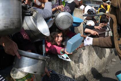 Palestinos hacen fila para conseguir comida durante la ofensiva aérea y terrestre en la Franja de Gaza, en Rafah