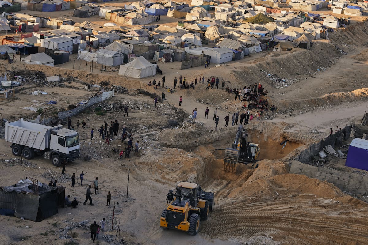Palestinos miran cómo maquinaria y algunos trabajadores egipcios buscan cuerpos de rehenes en ciudad Hamad, en Jan Yunis, en el sur de la Franja de Gaza, el lunes 27 de octubre de 2025. (AP Foto/Jehad Alshrafi)