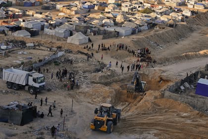 Palestinos miran cómo maquinaria y algunos trabajadores egipcios buscan cuerpos de rehenes en ciudad Hamad, en Jan Yunis, en el sur de la Franja de Gaza, el lunes 27 de octubre de 2025. (AP Foto/Jehad Alshrafi)