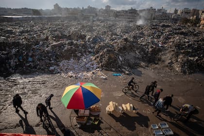 Palestinos pasan junto a montones de basura ardiendo en la Ciudad de Gaza, que no cuenta con sistema de recogida de basuras, el 12 de febrero de 2025