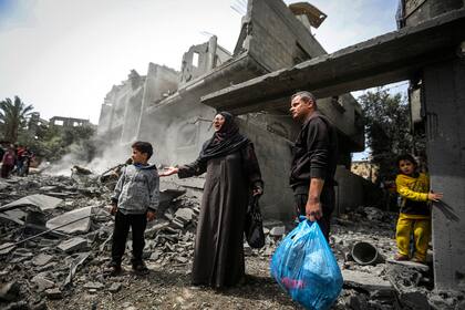 Palestinos recopilan sus pertenencias entre los escombros de un edificio residencial tras un ataque aéreo israelí en el campo de refugiados de Maghazi, en el centro de la Franja de Gaza, el 29 de marzo de 2024. (AP Foto/Ismael Abu Dayyah)