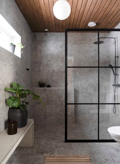 Para su baño optaron por revestimientos cerámicos que imitan la piedra natural y una mampara de hierro repartido hecha a medida para cerrar el box de ducha.