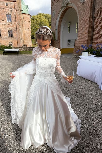 Para su gran día, Cecilie Juhl vistió un traje espectacular que se destaca por su trabajo de encaje floral sobre una figura encorsetada, con capa también de encaje. La cintura, bien definida, da paso a una falda de satén, cuya estructura cobra movimiento a través de amplios pliegues que desembocan en una imponente cola. Coronó su elección con la tiara floral de diamantes de la familia Egeskov, de la que caía un velo de tul de varios metros
