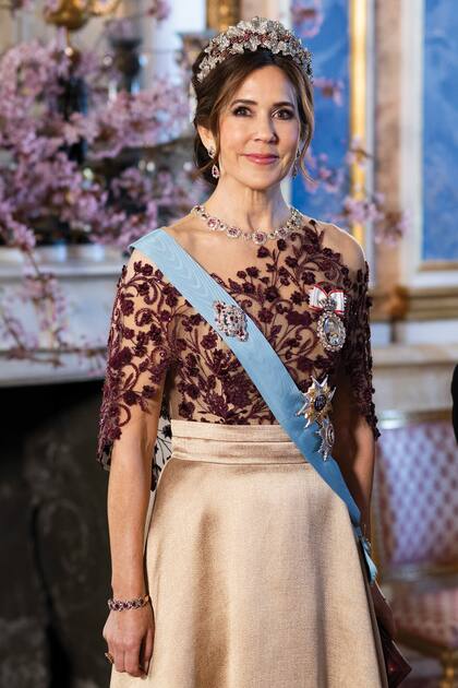 Para su primera comida de gala en el extranjero desde que es Reina, Mary recicló un espectacular conjunto del diseñador Jesper Høvring compuesto por falda satinada con fajín y top de corte asimétrico, con transparencias y pedrería, que se llevaba perfecto con el conjunto más importante de su joyero: tiara, collar, pendientes, pulsera y anillo de brillantes y zafiros en forma floral. También lució la orden de los Serafines, que esa misma mañana recibió de manos del monarca sueco.