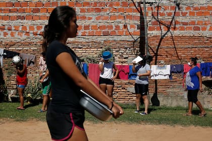 Las personas que agarran contenedores esperan en la fila para almorzar gratis en el vecindario "Bañado Sur" de Asunción. Las mujeres del vecindario cocinaron alimentos donados y se los sirvieron a otros residentes, muchos de los cuales trabajan como recicladores sin trabajo. en medio del e