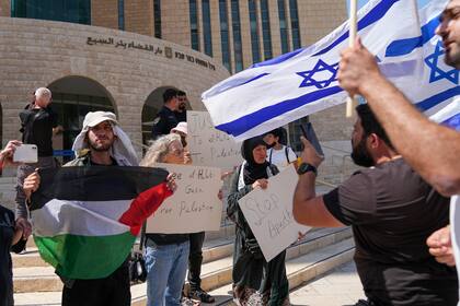 Partidarios de Mohammed el-Halabi llevan una bandera palestina y carteles mientras manifestantes israelíes ondean banderas de Israel en las afueras de la corte en la ciudad israelí de Beerseba el 15 de junio del 2022. La corte declaró al trabajador de ayuda culpable de varios cargos de terrorismo. (AP Foto/Tsafrir Abayov)