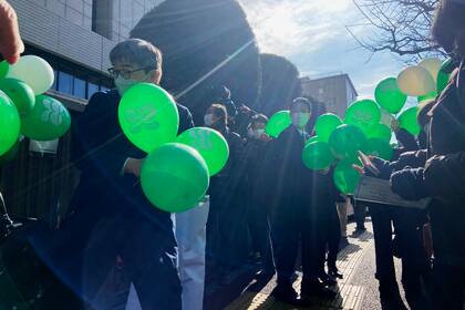 Partidarios de seis personas que denunciaron a la empresa que gestiona la plata de Fukushima tras desarrollar cáncer de tiroides luego del accidente nuclear, esperan con globos verdes en el exterior del Tribunal de Distrito de Tokio, el 27 de enero de 2022. (AP Foto/Mari Yamaguchi)