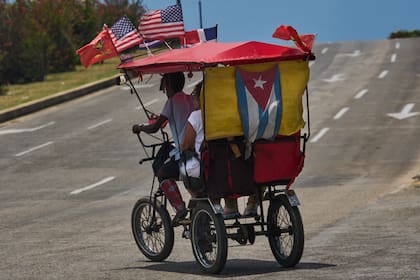 Pasajeros viajan en un bicitaxi adornado con las banderas de Estados Unidos, Cuba y la República Dominicana, en La Habana, Cuba