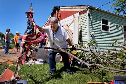 Patti Manley, de 69 años, retira una desgarrada bandera estadounidense mientras recoge ramas en el patio trasero de la casa de su madre en Morningdale Place en Mehlville, Misuri, el lunes 27 de mayo de 2024, después de una violenta tormenta y posible tornado ocurridos el domingo. (Robert Cohen/St. Louis Post-Dispatch vía AP)