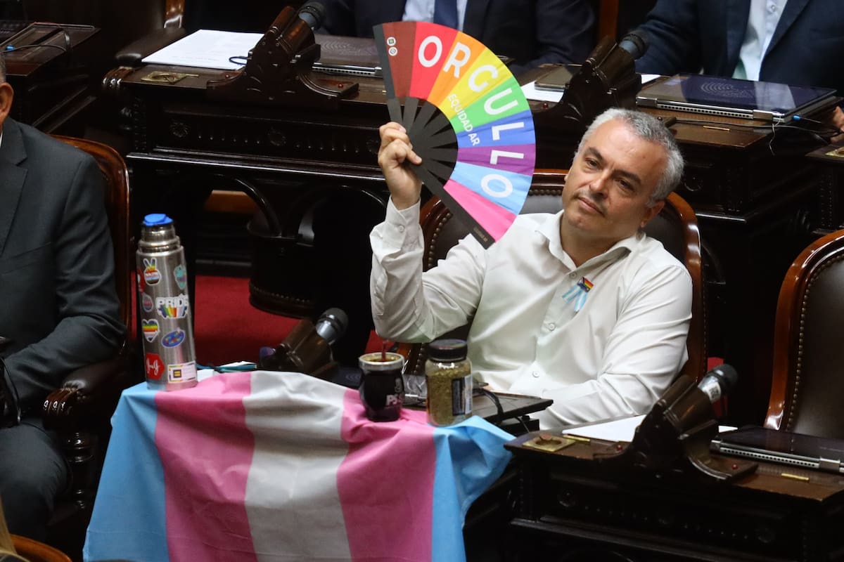 Paulón, con una bandera trans y un abanico arcoiris