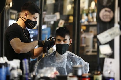 Peluquero y cliente, con barbijos y medidas de seguridad de por medio, en uno de los locales de The Barber Job