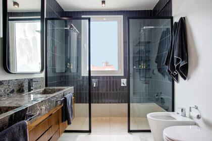 Pensando en la funcionalidad, la diseñadora de interiores Verónica Stegman instaló una ducha doble revestida con azulejos gris oscuro colocados en forma vertical. La mampara apoya directamente sobre el piso.
