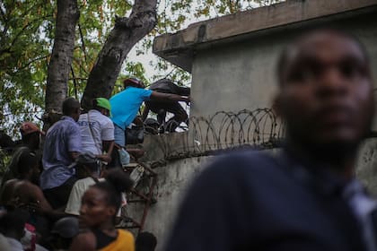 Periodistas se encaraman sobre una pared para evitar disparos de una pandilla en el Hospital General en Puerto Príncipe, en diciembre de 2024