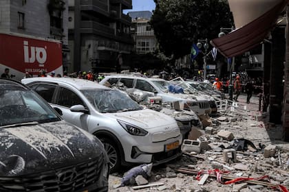 Personal de emergencia se encuentra detrás de vehículos dañados en una calle frente a un edificio alcanzado por un ataque con proyectiles iraníes en Ramat Gan, en el centro de Israel, el 6 de abril de 2026 (Foto de Ilia YEFIMOVICH / AFP)