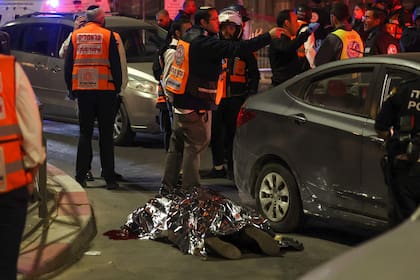 Personal de los servicios de emergencia y fuerzas de seguridad israelíes junto a un cadáver cubierto en el lugar donde se ha producido un atentado en un barrio de colonos de Jerusalén Este, anexionada por Israel, el 27 de enero de 2023.