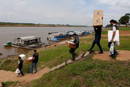 Personal electoral carga máquinas de voto y material electoral para llevar por barco a centros de votación, el día antes de la segunda vuelta de las presidenciales en Autazes, estado de Amazonas, Brasil, el sábado 29 de octubre de 2022. (AP Foto/Edmar Barros)