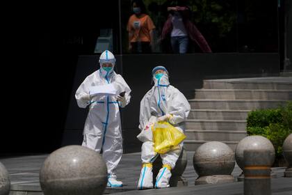 Personal médico con trajes de protección se toman un descanso tras hacer pruebas a residentes cerca de un complejo de oficinas, el jueves 12 de mayo de 2022 en Beijing. (AP Foto/Andy Wong)