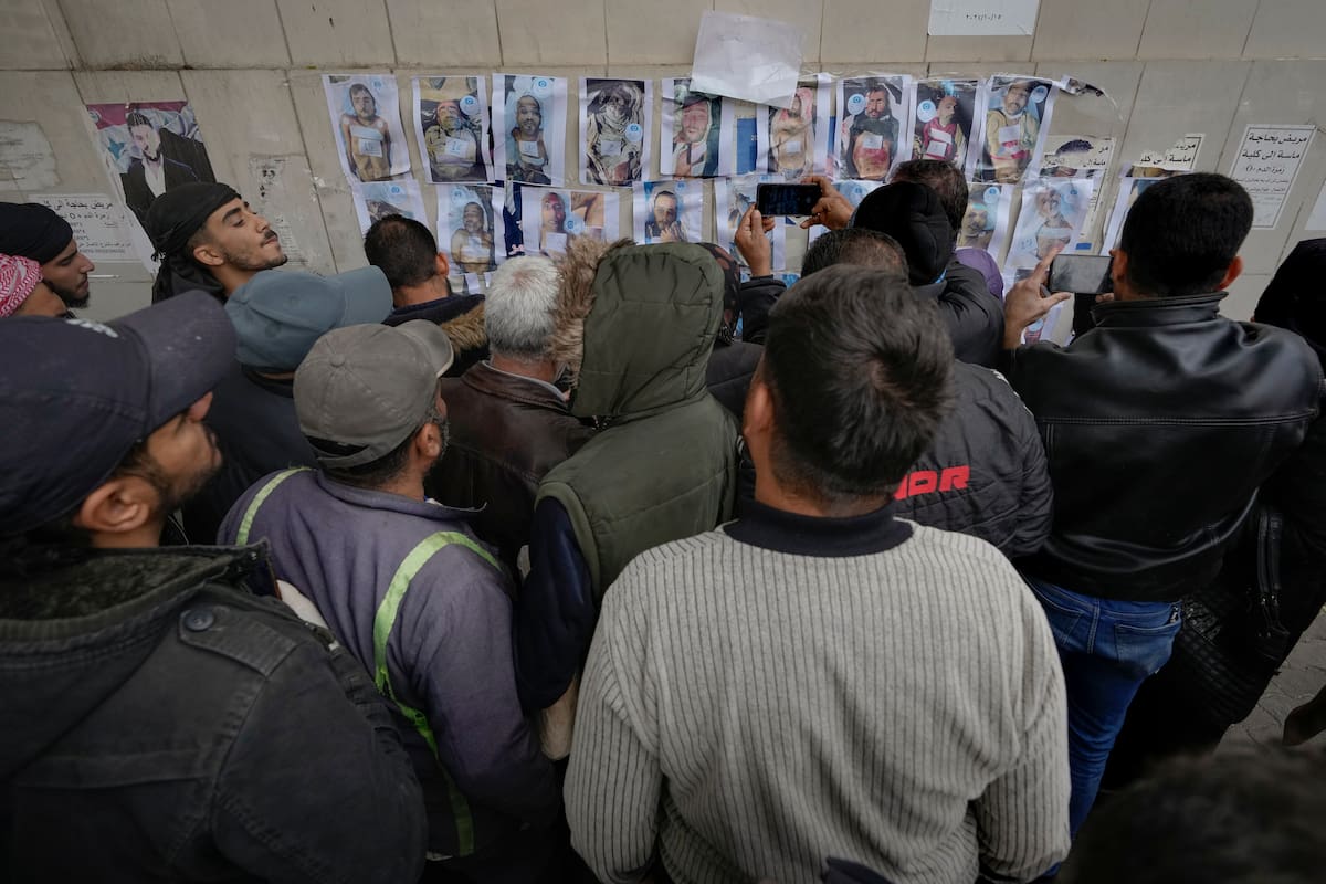Personas buscan en un muro con fotos a personas desaparecidas o fallecidas, afuera de la morgue del Hospital Al-Mojtahed, en Damasco, Siria. (AP Foto/Hussein Malla)