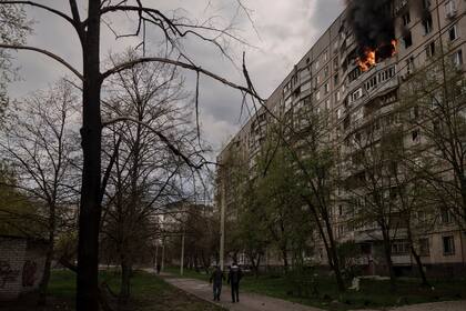 Personas caminan cerca de un inmueble en llamas después de que fuera impactado durante un bombardeo ruso en Járkiv, Ucrania, el viernes 22 de abril de 2022. (AP Foto/Felipe Dana)
