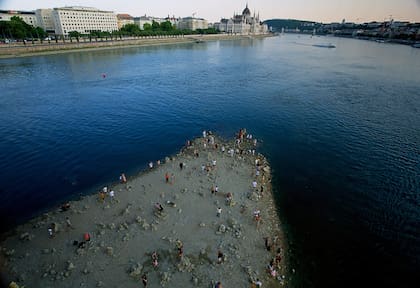 Personas caminan sobre un banco de arena bajo el Puente Margareth del río Danubio, en el centro de Budapest
