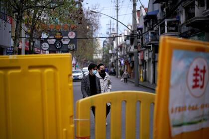 Personas con máscaras faciales caminan en un área residencial bloqueada por barreras en Wuhan