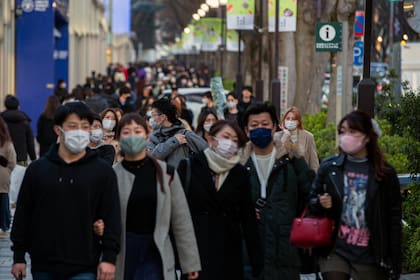 Personas con tapabocas para ayudar a frenar la propagación del coronavirus caminan por una vereda en un distrito comercial de Tokio, el domingo 28 de febrero de 2021