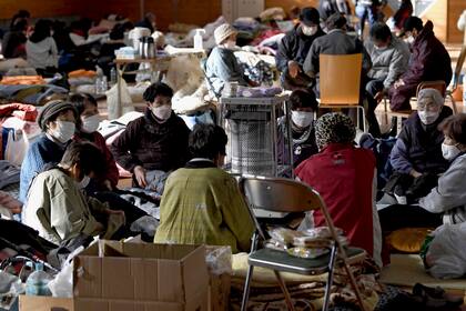 Personas evacuadas se calientan en un albergue el lunes 8 de enero de 2024, luego de un sismo en Anamizu, en la prefectura de Ishikawa, Japón. (Kyodo News via AP)