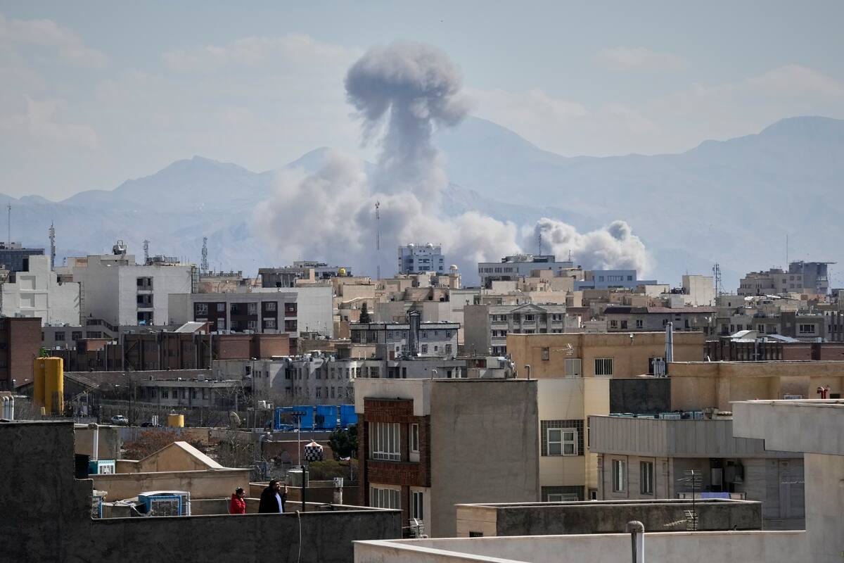 Personas observan desde una azotea mientras una columna de humo se eleva tras un ataque en Teherán, Irán, el domingo