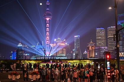 Personas que usan mascarillas como medida preventiva contra el coronavirus caminan por The Bund en Shanghai el 2 de noviembre de 2020, mientras se ve un espectáculo de luces en el distrito financiero de Lujiazu