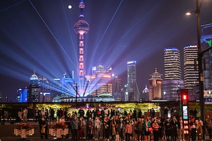 Personas que usan mascarillas como medida preventiva contra el coronavirus caminan por The Bund en Shanghai el 2 de noviembre de 2020, mientras se ve un espectáculo de luces en el distrito financiero de Lujiazu