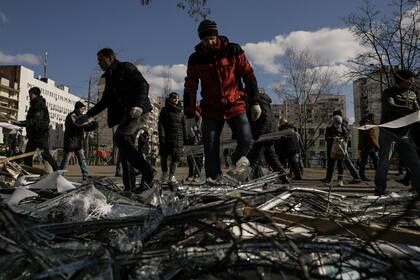 Personas quitan escombros afuera de un centro médico dañado luego de que partes de un misil ruso, derribado por la defensa aérea ucraniana, cayeran en un bloque de apartamentos cercano, según autoridades, en Kiev, Ucrania, el jueves 17 de marzo de 2022. (AP Foto/Vadim Ghirda)