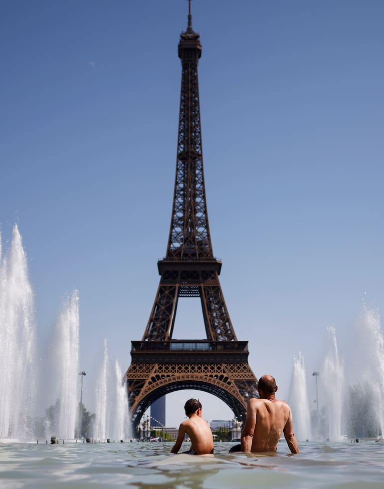 Personas se refrescan con agua de la fuente Varsovie, junto a la Torre Eiffel, durante una ola de calor en París, Francia, este martes
