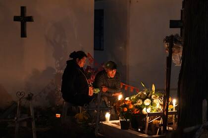 Personas sentadas junto a una tumba en el cementerio de San Gregorio Atlapulco durante las festividades del Día de Muertos en las afueras de la Ciudad de México, el miércoles 1 de noviembre de 2023. (AP Foto/Marco Ugarte)